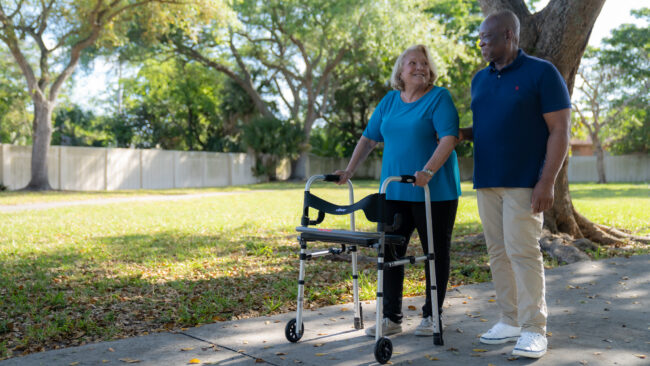 Senior woman with walker walking with men at park.