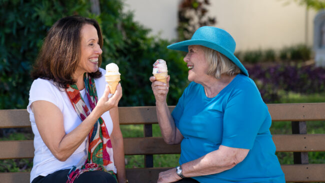 Senior women sitting in bench, smiling and eating icecream.