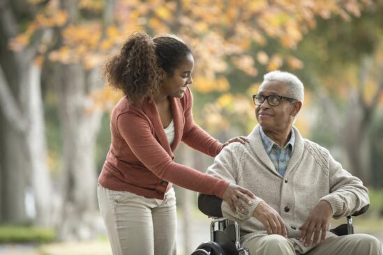 Young woman smiles and looks over older gentleman in wheelchair