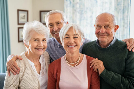 Portrait of happy elderly people looking at camera at care centre. Cheerful senior man and beautiful old woman embracing and posing for a photo. Smiling seniors standing together with a big grin on their faces at nursing home.