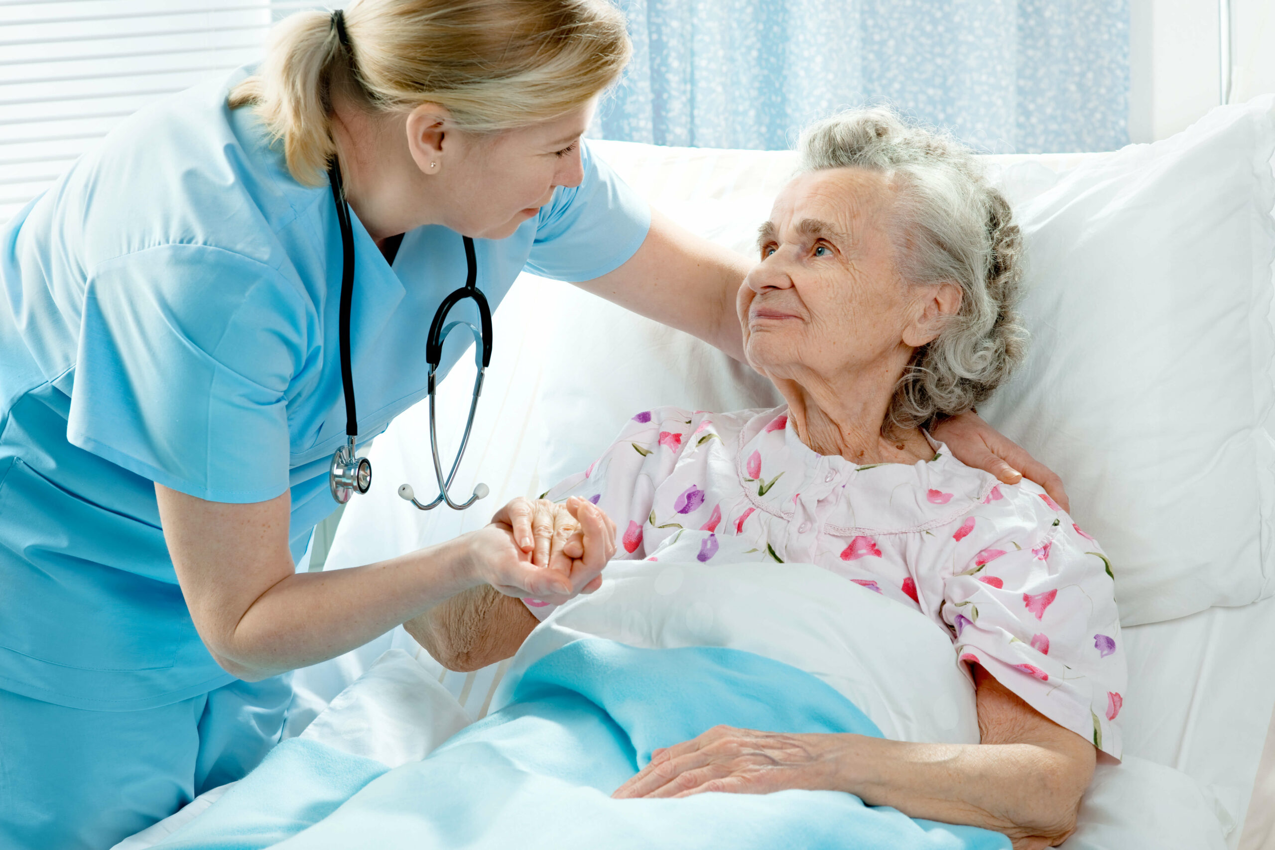 Nurse holding the hand of an older woman in a hospital bed