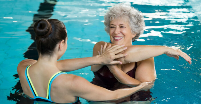 Senior retired woman staying fit by aqua aerobics in swimming pool.